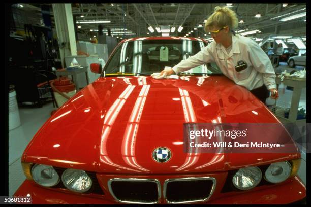 Female auto worker inspecting finish of shiny red BMW at new American plant which can produce cars for much less than it costs in Germany.