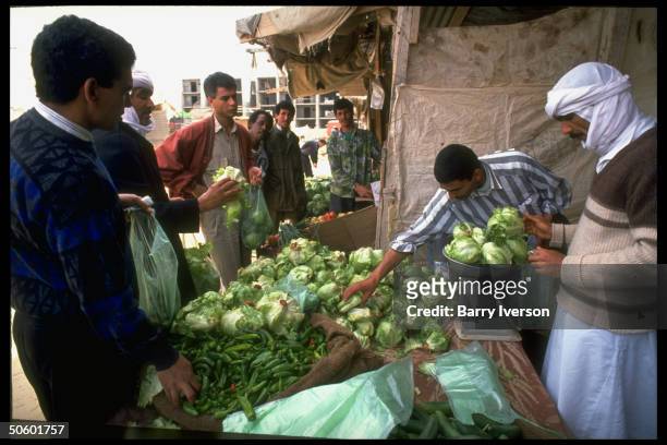 Shoppers buying long green peppers & heads of lettuce fr. Vegetable market stall.