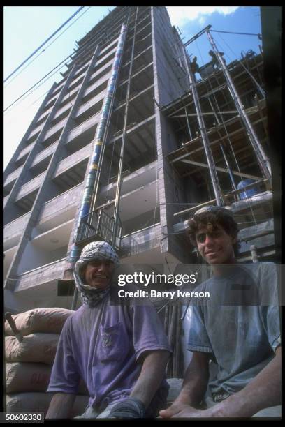 Workers taking break fr. Cement mixing, framed by highrise bldg. Under construction on Omar Mukhtar Street; Gaza City, Palestinian autonomous Gaza.