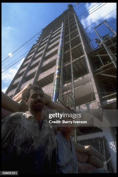 Workers taking break fr. Cement mixing, framed by highrise bldg. Under construction on Omar Mukhtar Street; Gaza City, Palestinian autonomous Gaza.