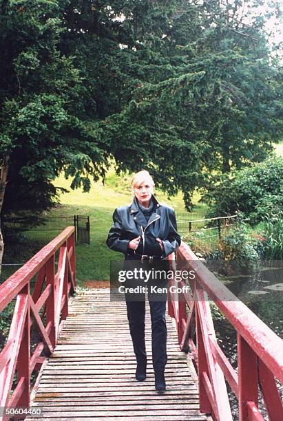 Singer Marianne Faithfull wearing expensive black leather jacket as she poses on bridge that crosses River Rye, outside her 19th C. Cottage.