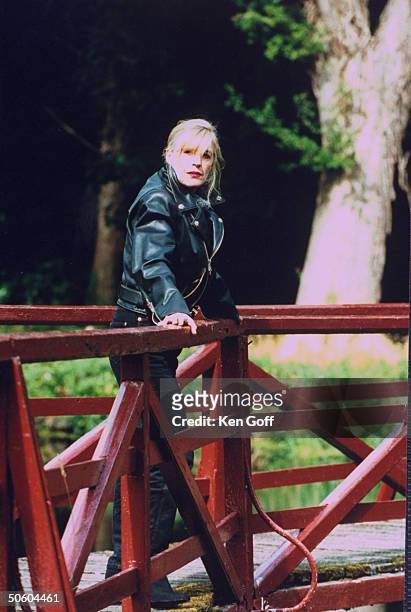 Singer Marianne Faithfull wearing black leather jacket as she poses on bridge that crosses River Rye, outside her 19th C. Cottage.