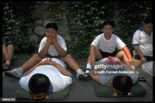 Boys performing paired exercises at weight loss camp for obese children aged 8-16, paying 780 yuan fee for 10-day stay.