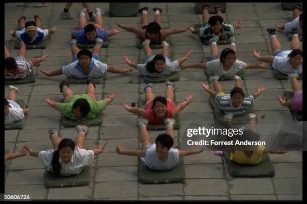 Boys & girls doing mat exercises at weight loss camp for obese children aged 8-16, paying 780 yuan fee for 10-day stay.