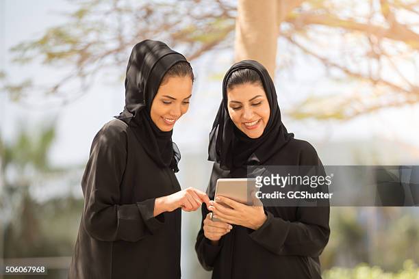 deux des émirats arabes unis pour les femmes ayant la discussion avec une tablette numérique - arab student kids photos et images de collection