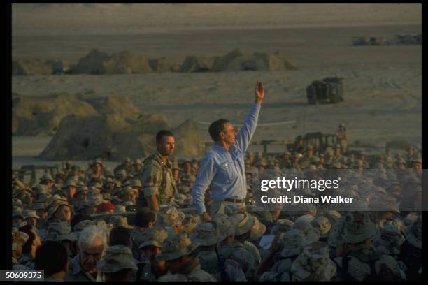 Pres. George Bush waving triumphantly, above crowd of First Marine Division desert command post marines, spending Thanksgiving w. American troops on...