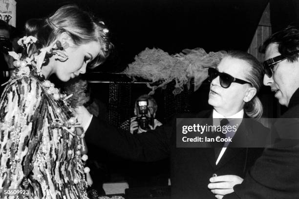 Fashion designer Karl Lagerfeld & assist. Gilles Du Four checking his trademark chains on his model Claudia Schiffer wearing his sequined evening...