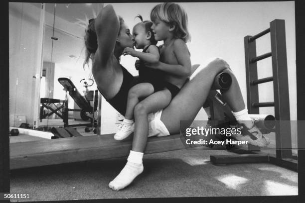 Tennis player Carling Bassett-Seguso, rebounding from bulimia, doing a sit-up on slantboard while kissing her 2-yr-old daughter Carling Jr. Who sits...