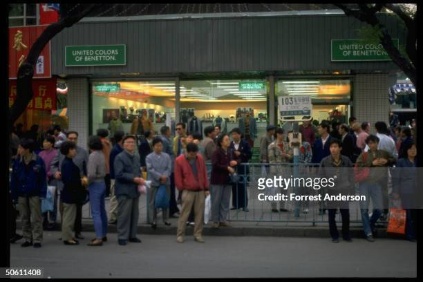 Locals waiting at bus stop by Benetton Italian clothing shop, 1 of many new stores in city, re economic reform as Communist Party Congress convenes.
