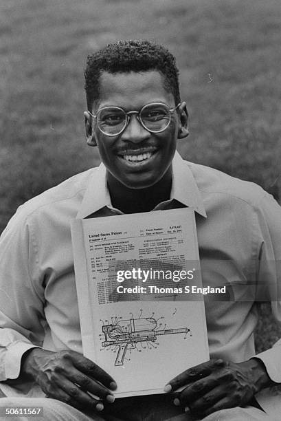 Lonnie Johnson, inventor of Super Soaker a large plastic pump-action water gun, holding US patent for his invention while sitting on grass outside...