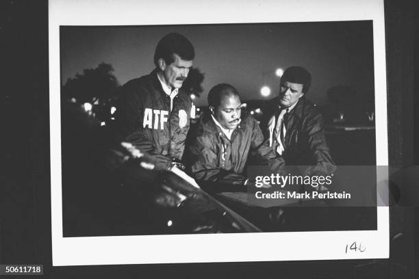 Fire agent Chuck Meyer w. Homicide sgts. John Jones & Mike Huckaby checking out info charts on hood of car at night as they spearhead the...