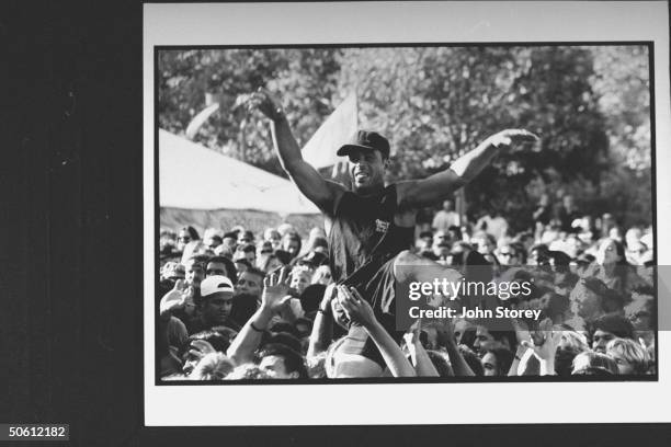 Packed crowd of youthful concertgoers passing an exuberant black male fan over their heads on a trip of jubilation during the Lollapolooza '92...