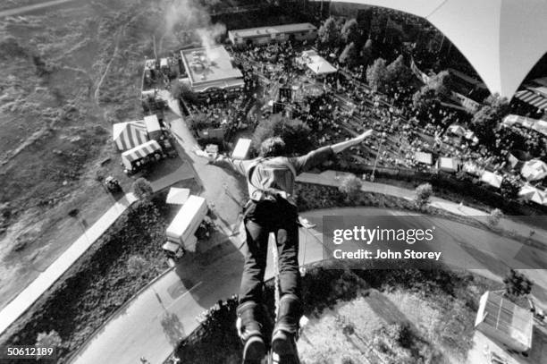 View looking down on a bungee jumper as he takes off from platform high above the carnival tents & crowd at the Lollapalooza '92 traveling rock fest...