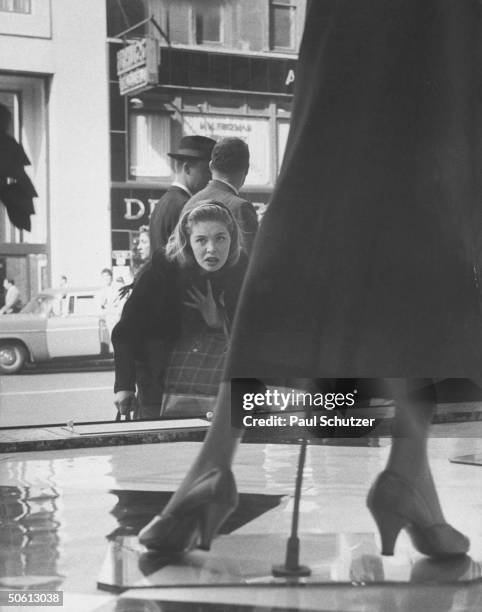 Young woman w. Dubious look on her face, gazing into Bloomingdale's window, where Dior-inspired longer skirts are being displayed.