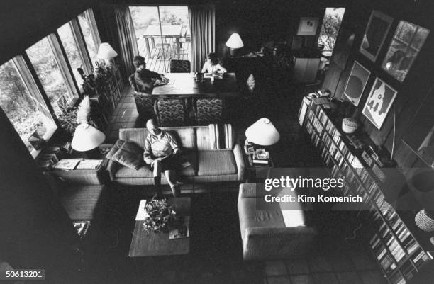 Large dining room/living room area w. Very long bookcase full of books running along one wall where backwoods author David Colfax reads magazine on...