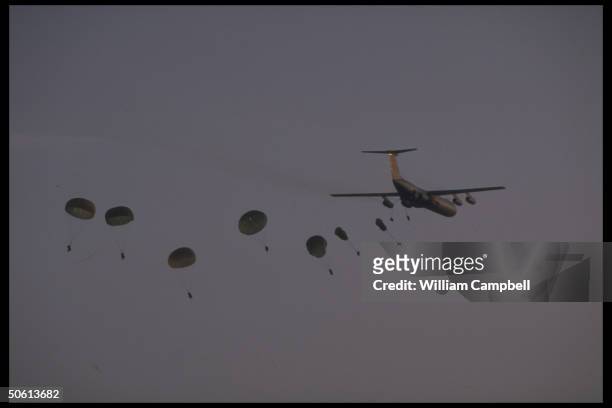 Air Force C-141 leaving parachutes in its wake as US 18th Airborne Corps paratroopers jump fr. Transport plane, in training exercise, at Fort Bragg.