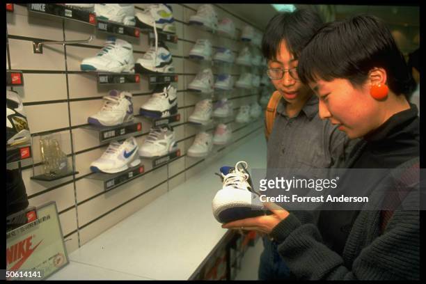 Young couple admiring sneaker fr. Nike display, popular Amer. Brand mfg. Shoes in China for domestic & export markets, at dept. Store in Beijing,...