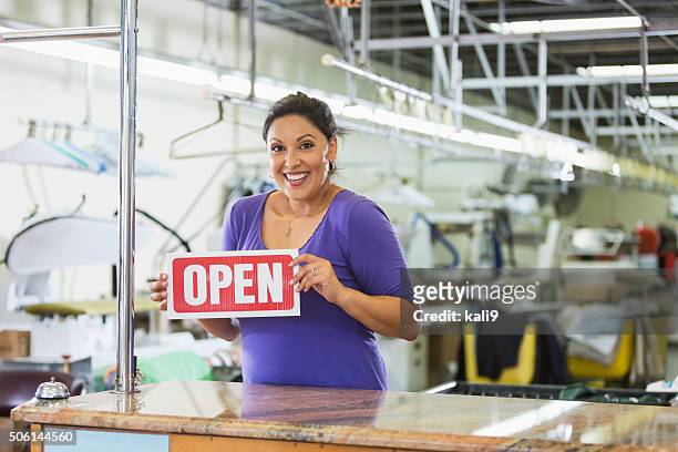 hispanic woman working in a dry cleaner with open sign - store opening stock pictures, royalty-free photos & images