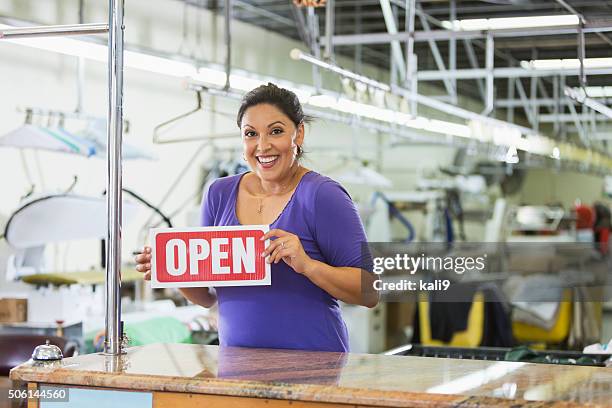 hispanic woman working in a dry cleaner with open sign - butiksinvigning bildbanksfoton och bilder