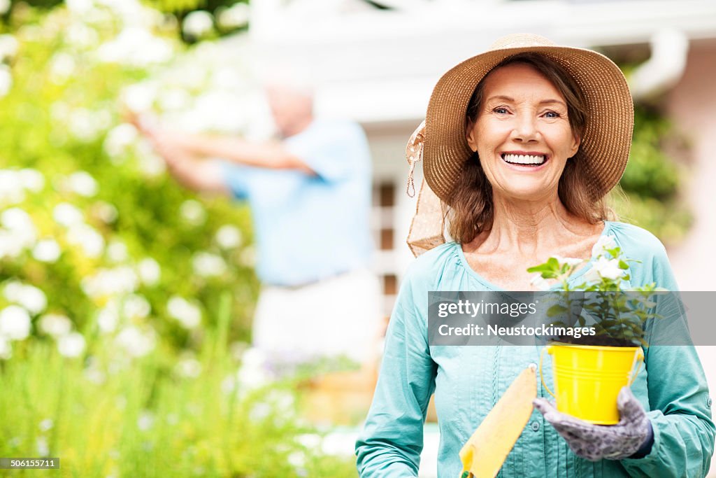 Senior Frau hält Blumentopf und Schaufel und Mann Gartenarbeit