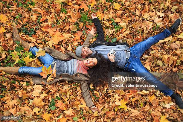 sonriente pareja acostado en hojas alfombra - noviembre fotografías e imágenes de stock