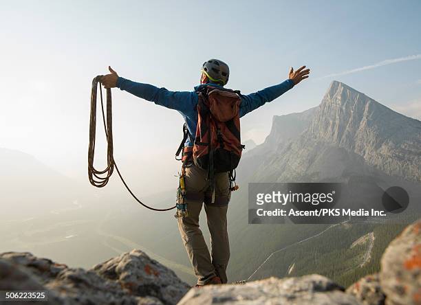 climber stands on summit rocks, arms outstretched - bergsteiger gipfel stock-fotos und bilder