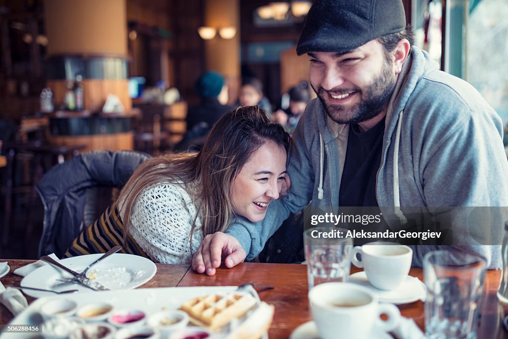 Happy Young Couple Drinking Coffee and Laughing in Cafe