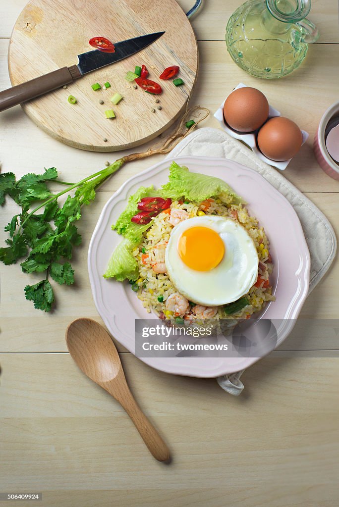 Asian style seafood fried rice with sunny side up egg on wooden kitchen counter top.