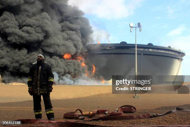 Libyan fireman stands in front of smoke and flames rising from an oil storage tank at an oil facility in northern Libya's Ras Lanouf region on...