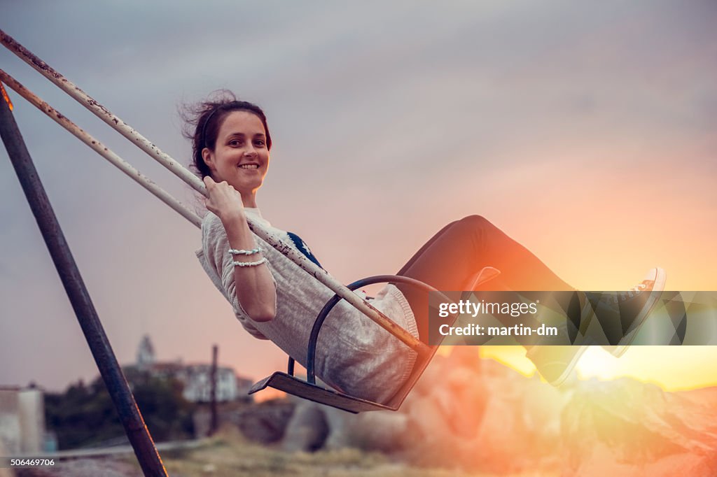 Joyful woman swinging at sunset