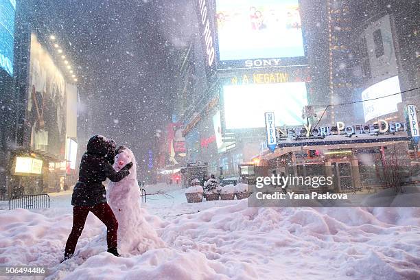 Woman decorates a snowman in Times Square as all cars but emergency vehicles are banned from driving on the road on January 23, 2016 in New York...