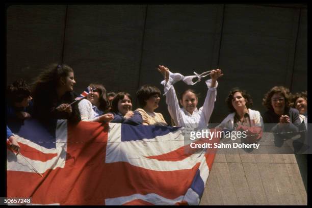 Crowd of wellwishers w. Union Jack draped on dock as Army wife holds out bra to entertain troops sailing to Falklands on QE2