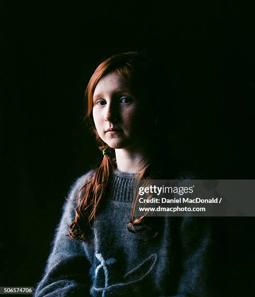 Dramatic portrait of young redheaded girl in soft window light with black background