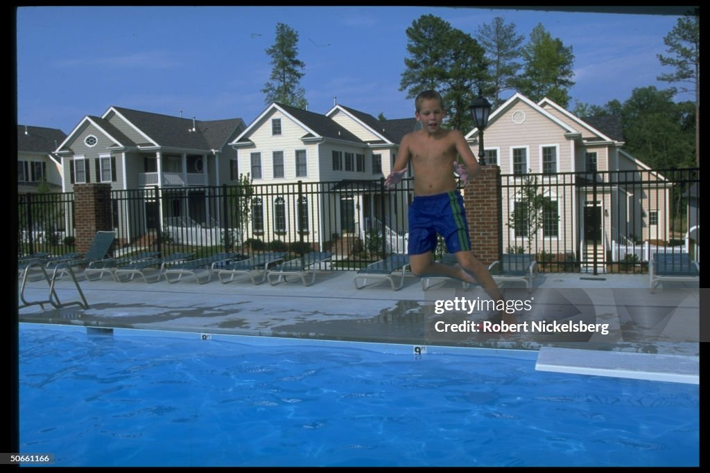 Boy jumping off diving board into pool a