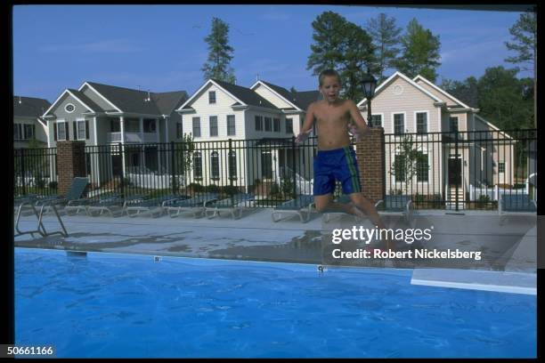 Boy jumping off diving board into pool at Southern Village, 300-acre suburban development designed to resemble small town w. Community-shared...