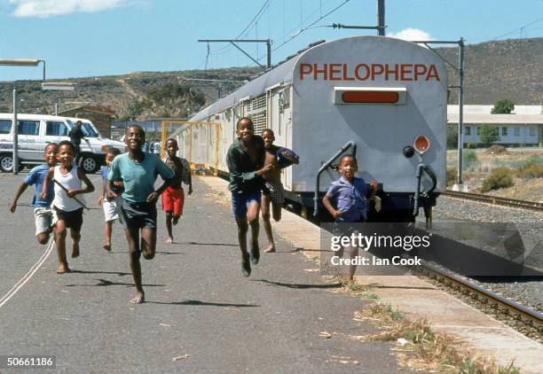 Black South African children running alongside tracks where medical train Phelophepa, founded by white South African Lynette Coetzee to bring...