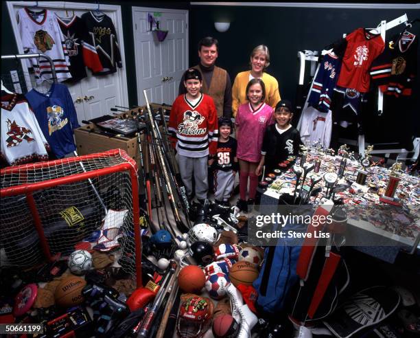 John & Kathy Glennon posing w. Their children in room filled w. Equipment, trophies, memorabilia & games that coincide w. Their various sporting...