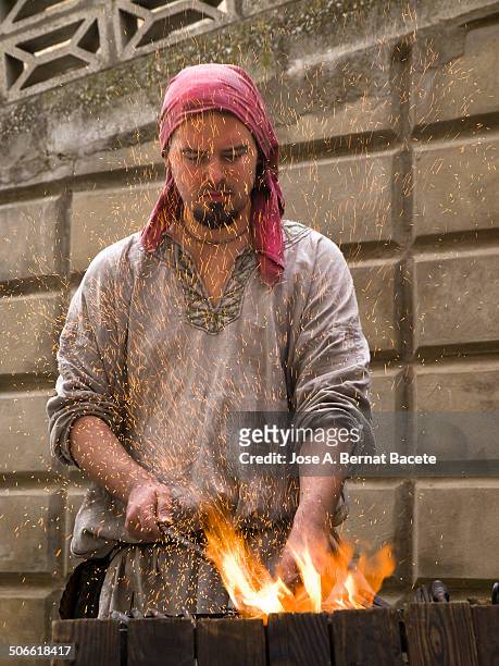 Blacksmith in a forge with fire and sparks on her face, in a medieval street market. Bocairent, , Spain