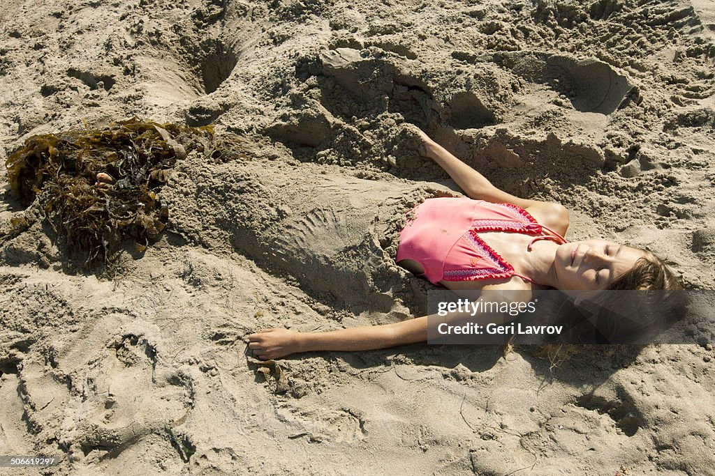 Young girl covered in a sand at a beach