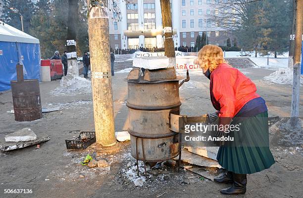 Woman places a wood into a stove on a street as opponent Moldovans stage an anti-government protest, demanding resignation of the government and...