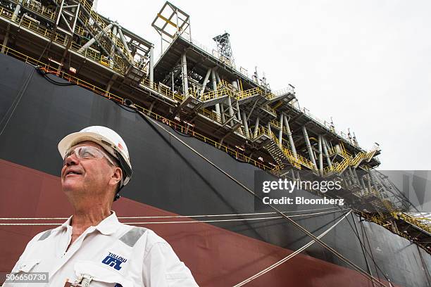 Worker stands dockside next to the Tullow Oil Plc Prof. John Evans Atta Mills Floating Production Storage and Offloading vessel at the Sembcorp...