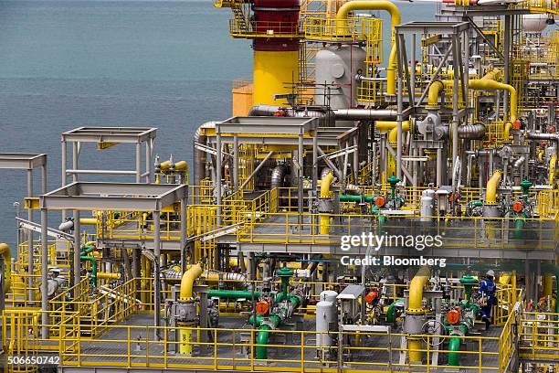 Worker, bottom right, walks on the Tullow Oil Plc Prof. John Evans Atta Mills Floating Production Storage and Offloading vessel docked at the...