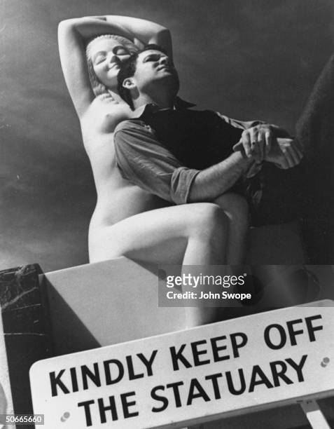 Man resting against statue of nude woman behind sign that says Kindly Keep off the Statuary at Hearst Castle.