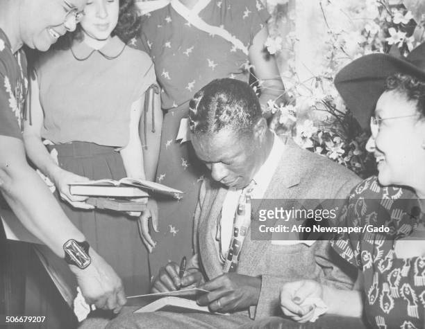 Singer and Jazz musician Nat King Cole signing autographs, 1953.
