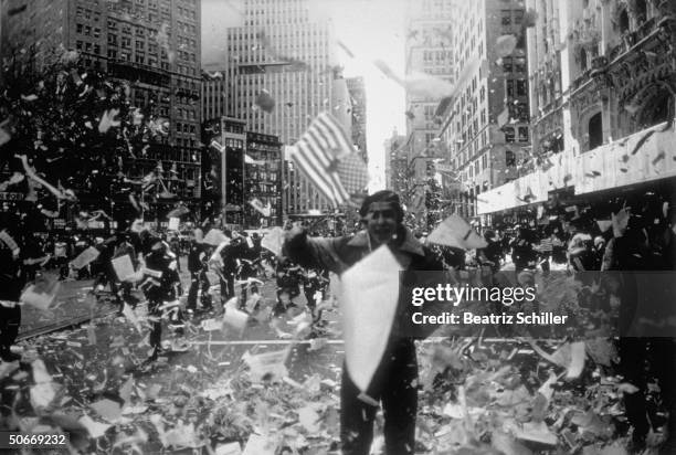 Celebrant waving flag amid shower of confetti during ticker tape parade on lower Broadway feting release of American hostages after 444 days of...