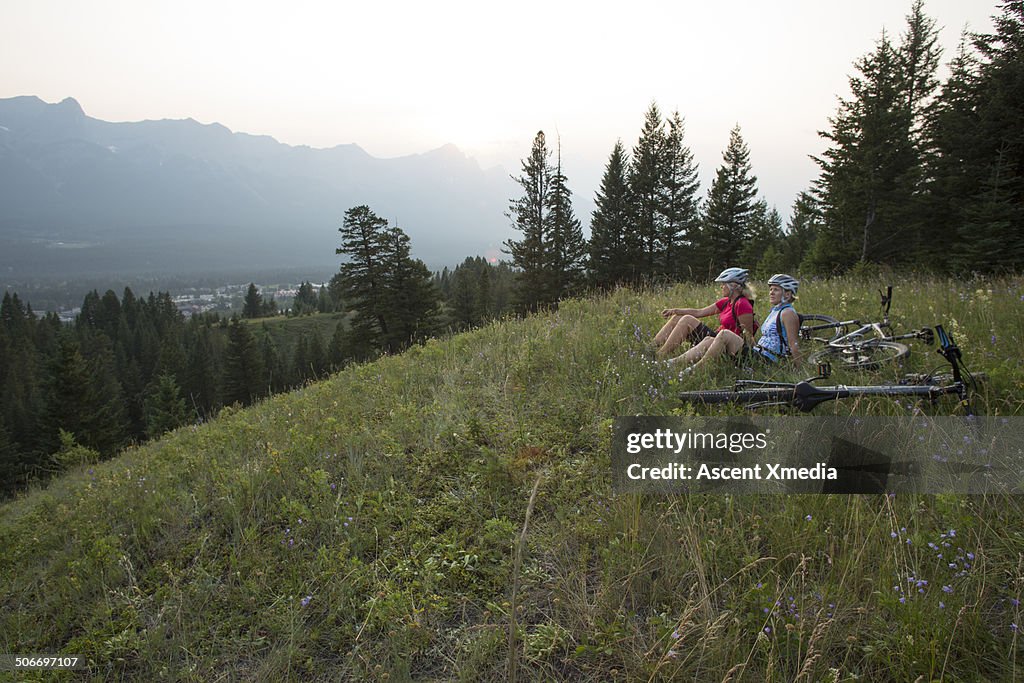 Female mountain bikers relax in mountain meadow