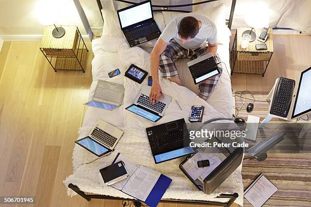 man sat on bed surrounded by computers - person surrounded by computer screens stock pictures, royalty-free photos & images