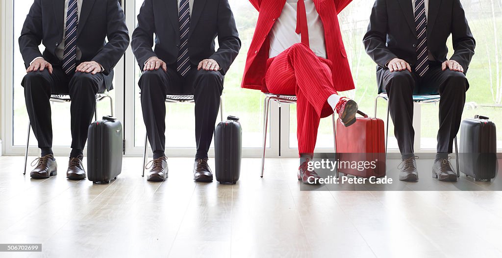 Four men on chairs, three black one red suit