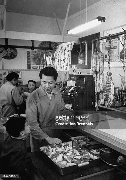 Interior of Chinatown butcher shop, small meat cuts and sausages hanging by hooks, English and Chinese signs, young Chinese butcher standing by cash...