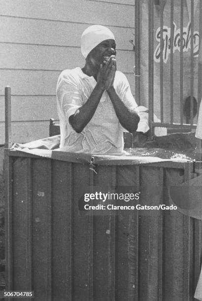 African-American woman wearing skullcap, smiling and wading in an aboveground pool, San Francisco, California, 1980.